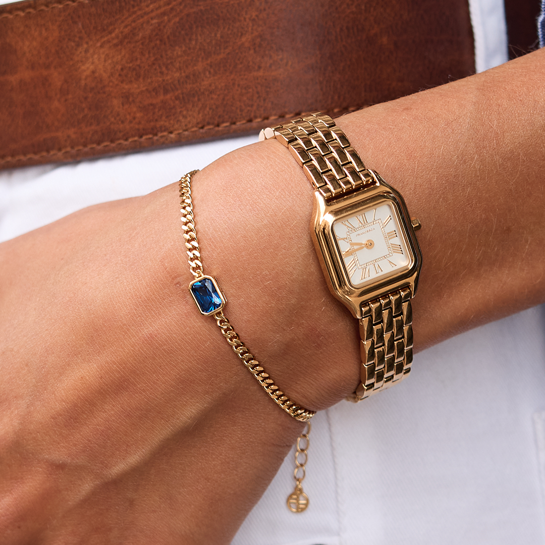 gold chain bracelet with a navy blue cubic zirconia bezel set close up on wrist next to watch