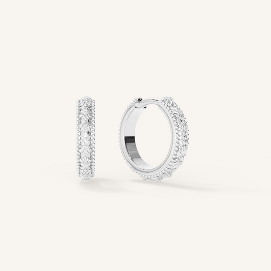 intricately designed silver hoops on white background