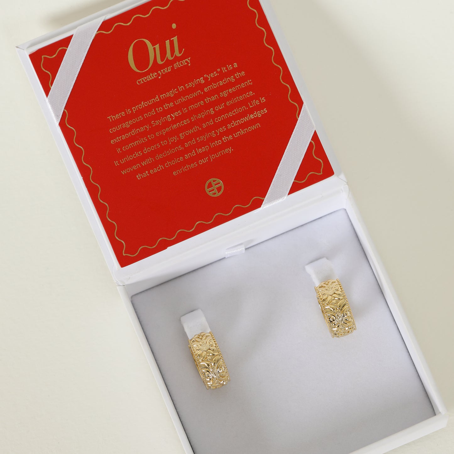 intricately designed statement gold hoops in white box with red and god charm card 