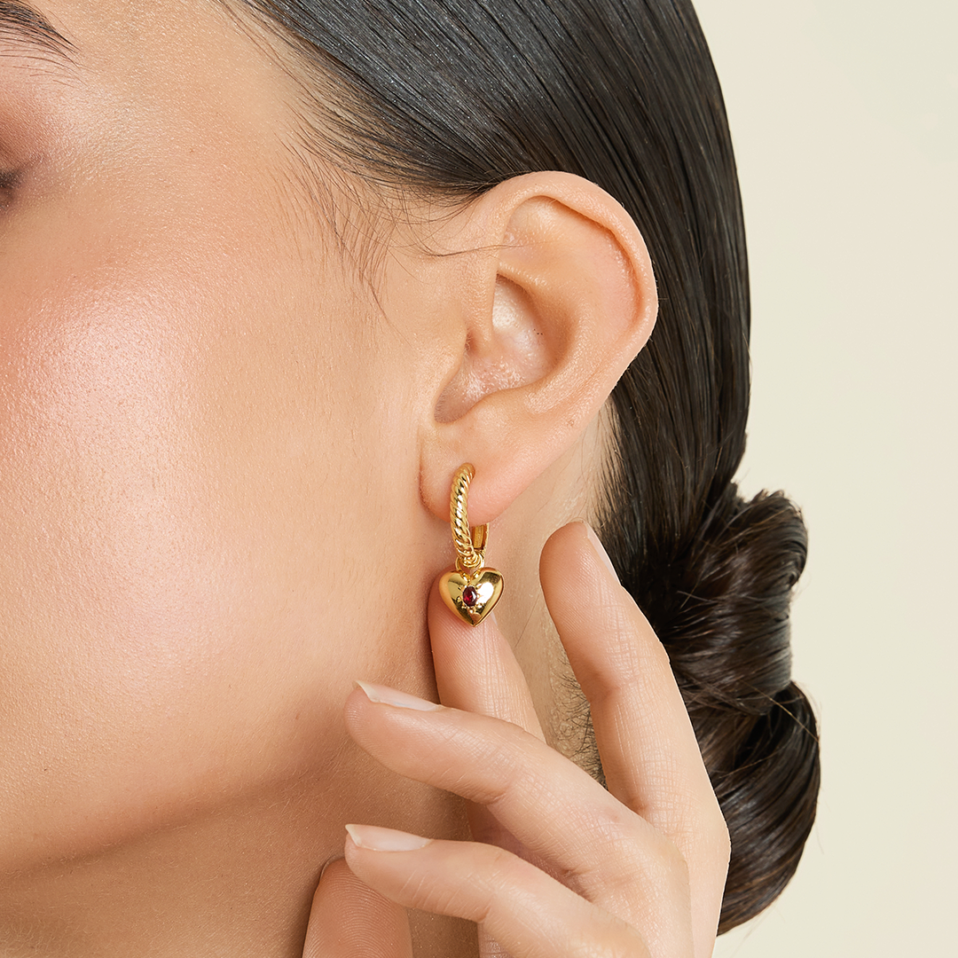 gold delicate hoops with a twist design with heart shaped hoop charms close up on ear 
