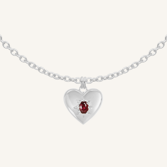 silver heart shaped charm with deep red oval cubic zirconia on plain chain on white background