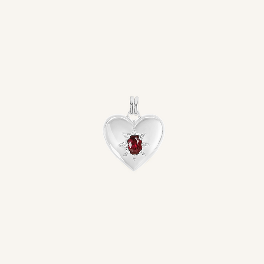 silver heart shaped charm with deep red oval cubic zirconia on white background
