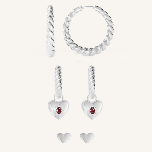 silver delicate hoops with a twist design silver huggies with heart shape hoop charms with red cubic zirconias with heart shaped studs on white background