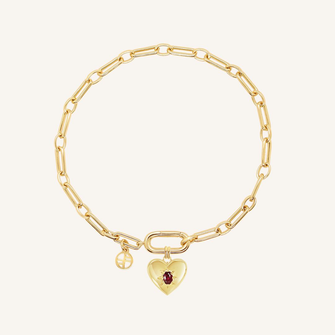 gold heart shaped charm with deep red oval cubic zirconia attached to create link bracelet on white background