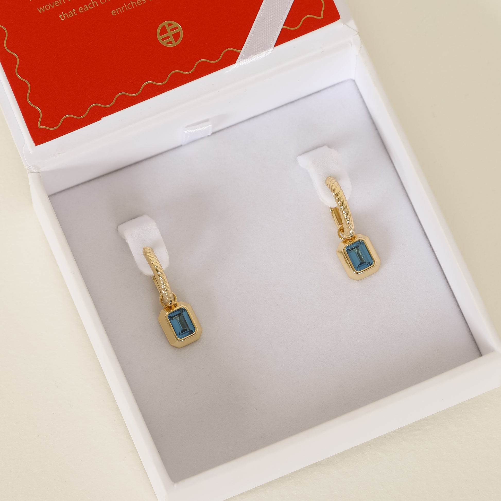 Gold hoops with Blue emerald cut cubic zirconias bezel set Inspired by the halls of Versailles on white earring box 