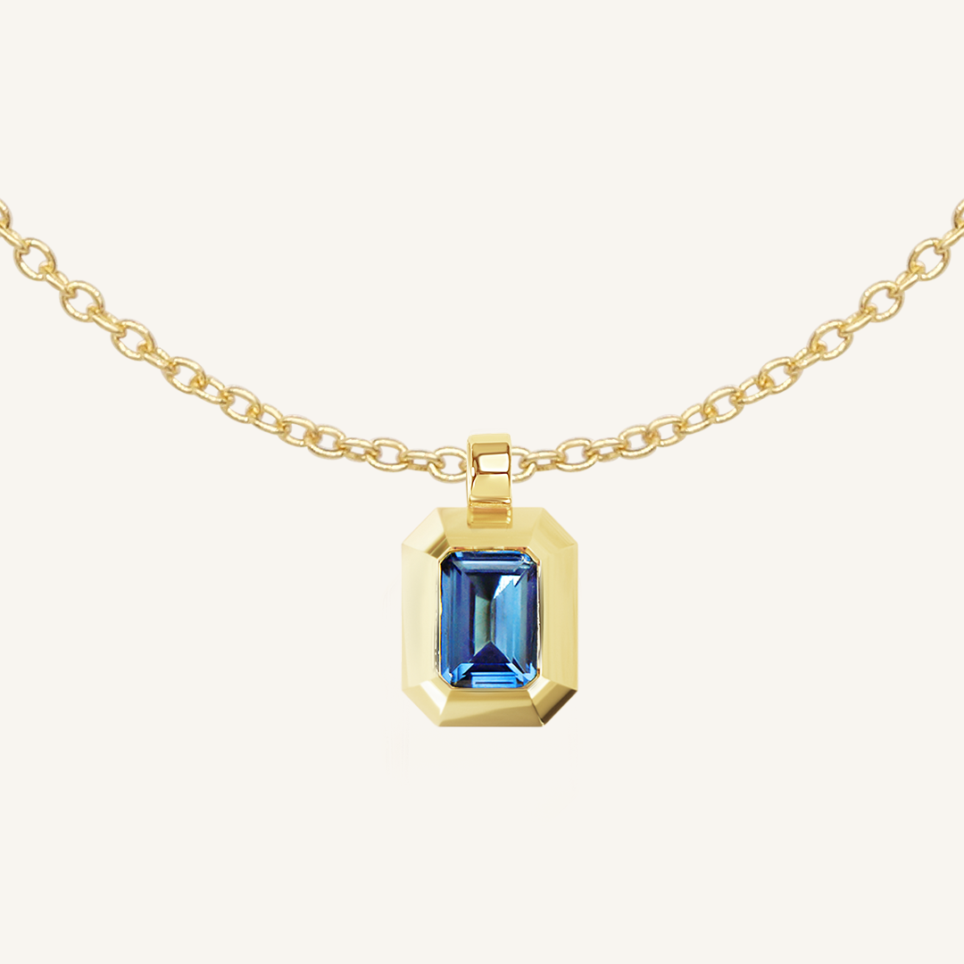 Gold charm with Blue emerald cut cubic zirconia bezel set Inspired by the halls of Versailles on plain chain on white background 