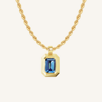 Gold charm with Blue emerald cut cubic zirconia bezel set Inspired by the halls of Versailles on rope chain on white background 