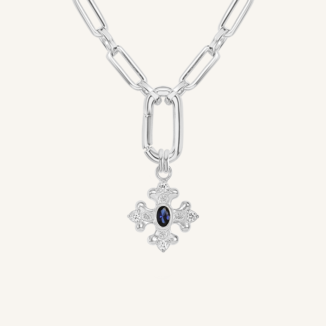 silver charm that features the intricate fleur-de-lis details found in the iconic Palace of Versailles accompanied by the deep blue stone on link chain on white background