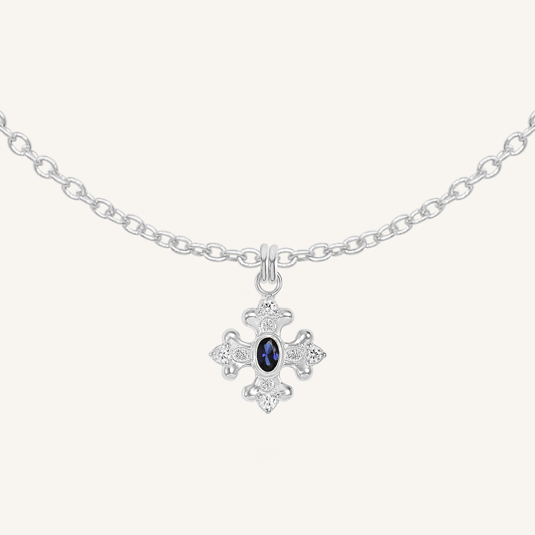 silver charm that features the intricate fleur-de-lis details found in the iconic Palace of Versailles accompanied by the deep blue stone on plain chain on white background