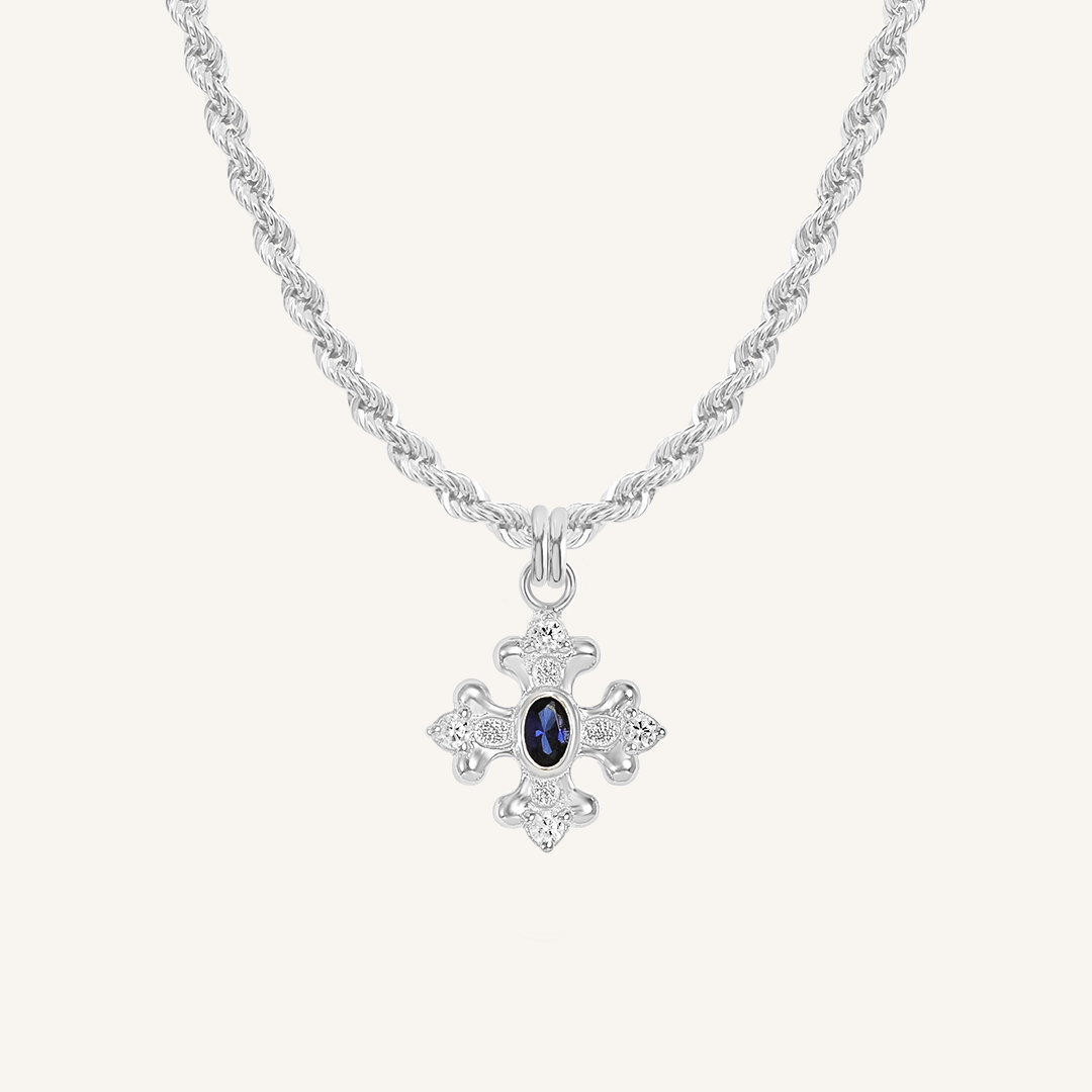 silver charm that features the intricate fleur-de-lis details found in the iconic Palace of Versailles accompanied by the deep blue stone on rope chain on white background