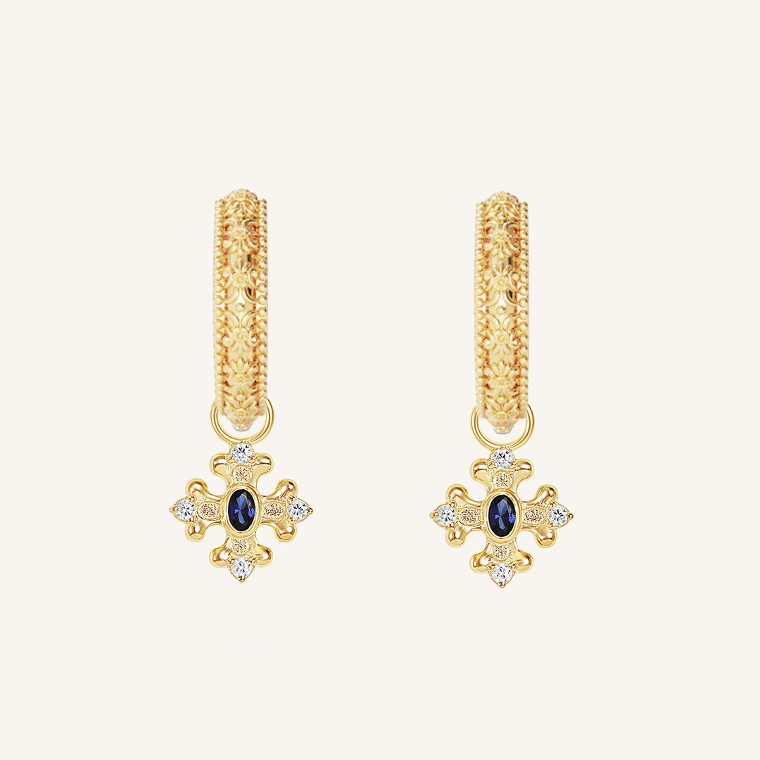 gold charm that features the intricate fleur-de-lis details found in the iconic Palace of Versailles accompanied by the deep blue stone on gold hoops on white background