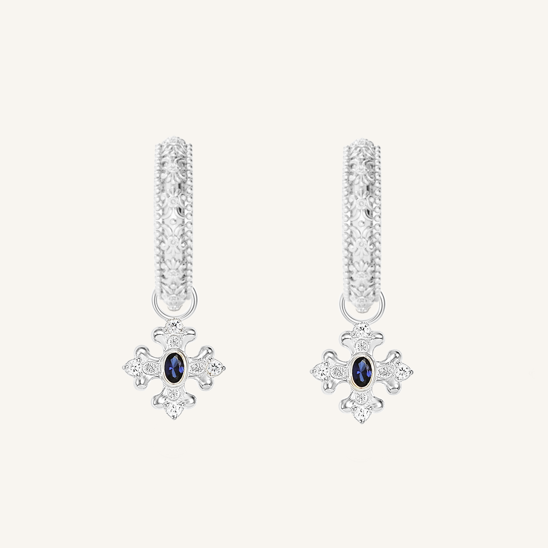 silver charm that features the intricate fleur-de-lis details found in the iconic Palace of Versailles accompanied by the deep blue stone on gold hoops on white background