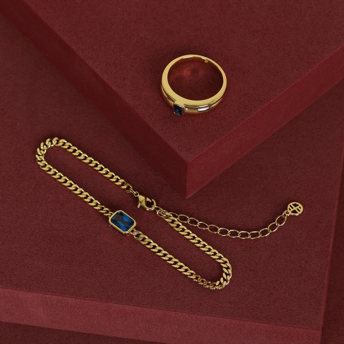 gold chain bracelet with a navy blue cubic zirconia bezel set in a set with gold ring with navy blue cubic zirconia  on red background